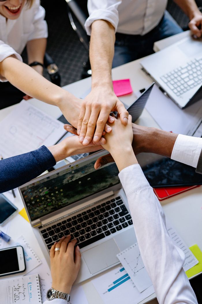 Home A diverse group of professionals stacking hands over a table symbolizing teamwork and collaboration.