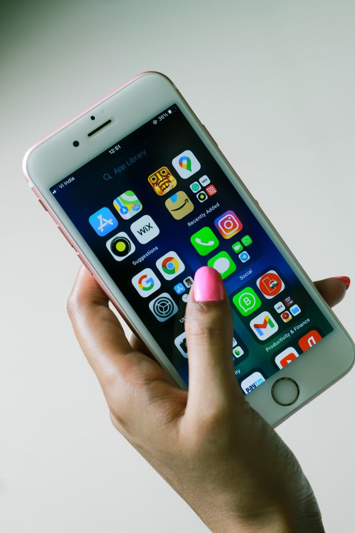 Close-up of a hand holding a smartphone displaying various apps on the screen.